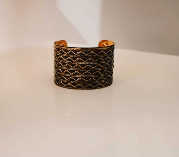 Black wrist cuff with brass wave pattern