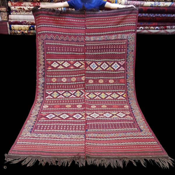 Persian Jajim Kilim Rug man is holding a kilim rug , the colours are maroon