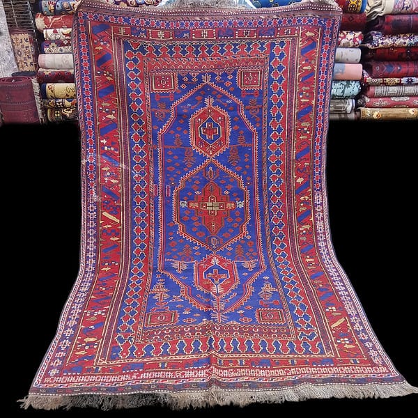 Kilim Rug from Afghanistan made by the Balouchi tribe photo shows the rug being held by a man, the rugs are vibrant blue creams reds etc.