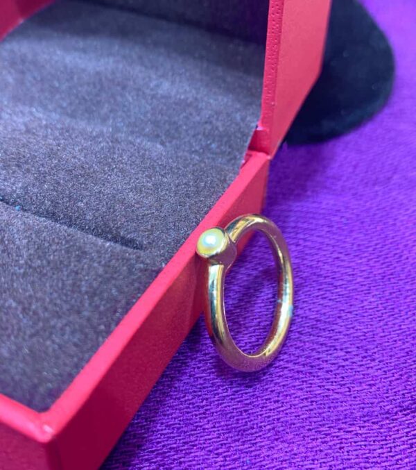Close-up of a stylish pearl and gold ring resting on a purple fabric surface, showcasing elegant jewelry design suitable for both women and men.