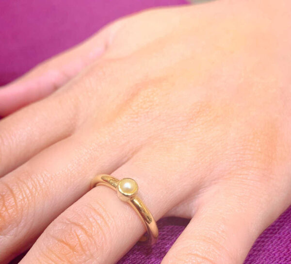 Gold ring with pearl detail on finger, showcasing elegant jewellery design.