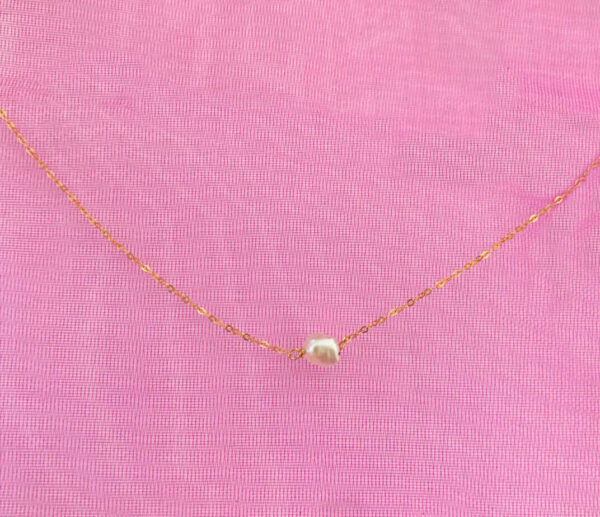 Pearl necklace with a single white pearl pendant on a delicate gold chain, displayed on a pink textured background. Perfect for elegant accessories and jewellery shopping.