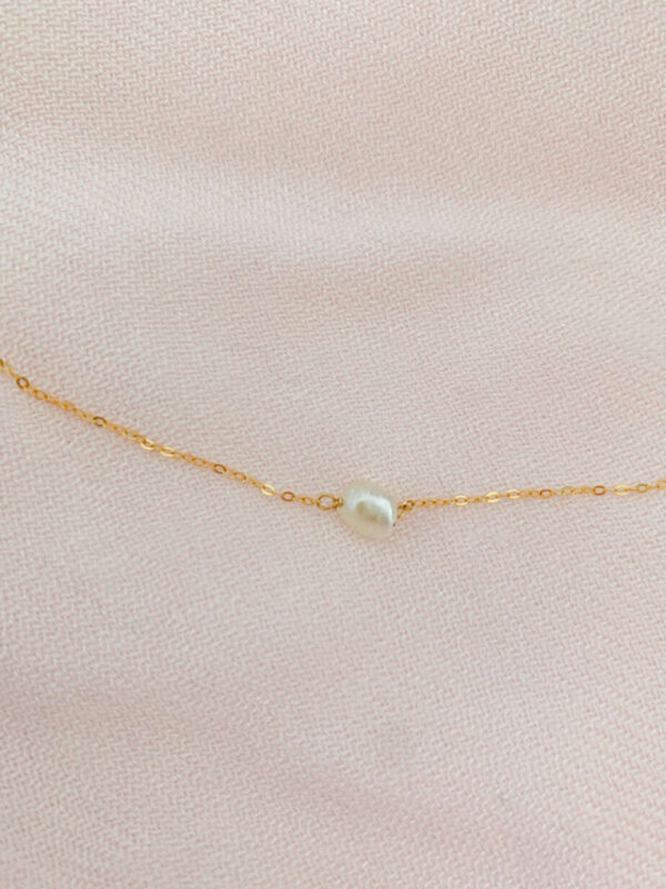Pearl necklace featuring a single white pearl on a delicate gold chain, displayed on soft pink fabric. Perfect for elegant jewellery collections and special occasions.