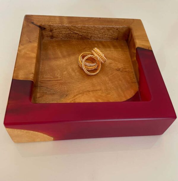 Jewellery display tray with wooden interior and red resin border, showcasing gold rings.