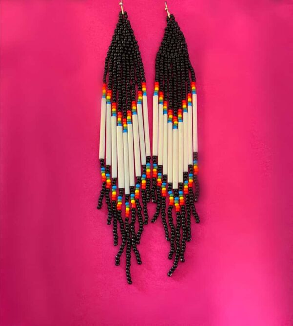 Beaded Native American-style earrings featuring black beads, colourful beads, and white elongated beads, hanging against a vibrant pink background. Perfect for traditional or bohemian fashion accessor.