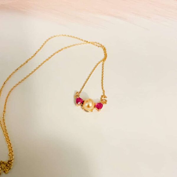 Gold necklace featuring pink gemstones and a central pearl, perfect for stylish accessories and jewellery collections.