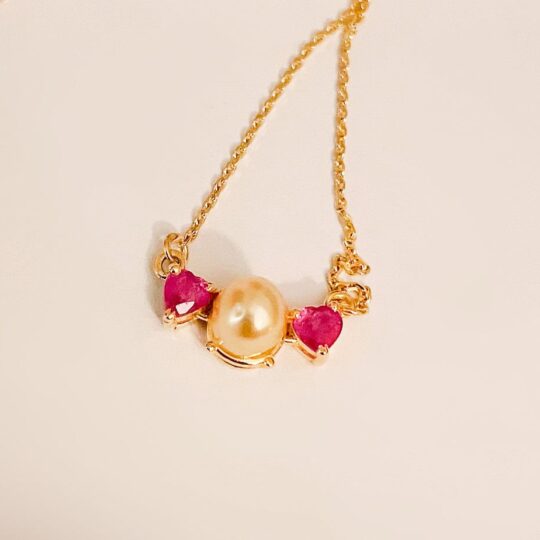 large natural pearl with 2 rubies on either side of a gold necklace.