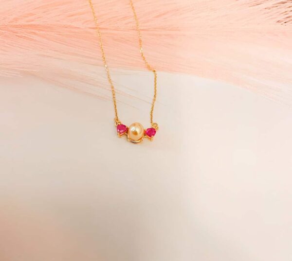 Elegant gold necklace featuring a central pearl flanked by vibrant rubies, perfect for special occasions and adding a touch of luxury to any outfit.
