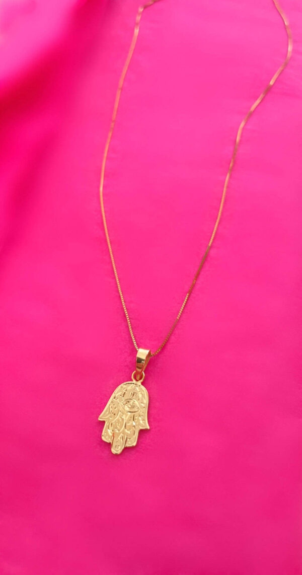 Elegant gold Hamsa hand pendant necklace displayed on vibrant pink fabric, symbolising protection and good luck, perfect for fashion accessories and spiritual jewellery.