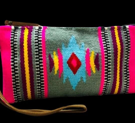 Brightly coloured ethnic pattern clutch bag with geometric designs in pink, blue, yellow, and black on a grey background, featuring a wrist strap for easy carrying.