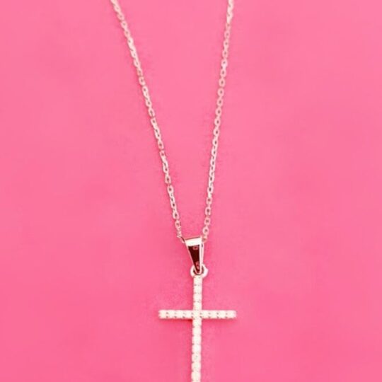 Delicate silver cross pendant necklace with sparkling embedded stones on a pink background, perfect for faith-inspired jewellery and stylish accessory shopping.