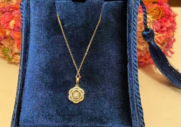 Shiny gold flower pendant necklace displayed in a luxurious navy blue jewellery box, perfect for gift giving or special occasions. Elegant jewellery piece with intricate design.