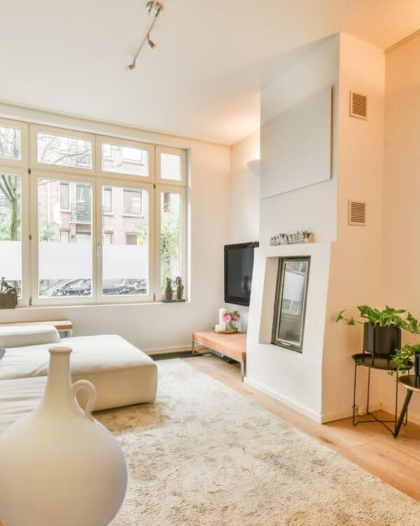 in the corner of the room is a large Arabian water jug set in a bright modern living room with large window, beige sofa, wall-mounted TV, indoor plants, and minimalist decor, perfect for cosy home aesthetic and everyday comfort.