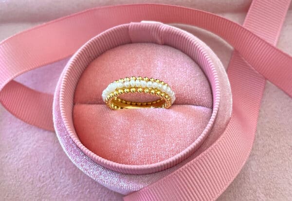 A beautiful gold ring adorned with lustrous pearls, displayed inside a plush pink velvet jewellery box with a satin ribbon, perfect for jewellery gifting or collection.