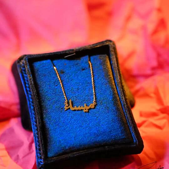 Delicate gold necklace with Arabic name inscription, presented in elegant black velvet box, perfect for special occasions or as a meaningful gift.