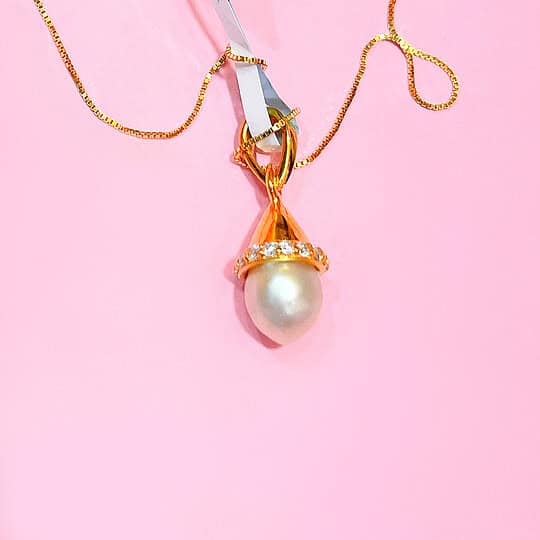 Close-up of a gold necklace featuring a large pearl pendant accented with sparkling diamonds on a pink background. Perfect for jewellery lovers seeking luxury and elegance. The natural large pearl is from Bahrain