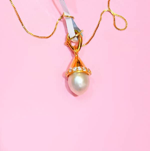 Close-up of a gold necklace featuring a large pearl pendant accented with sparkling diamonds on a pink background. Perfect for jewellery lovers seeking luxury and elegance. The natural large pearl is from Bahrain