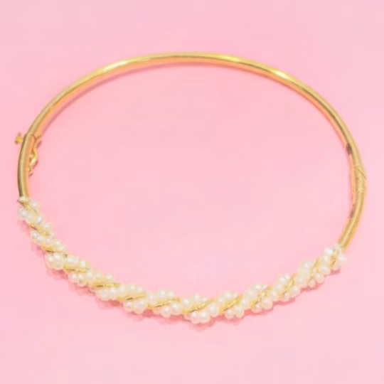 A stunning gold bangle with natural pearls from Bahrain displayed on a pink background.